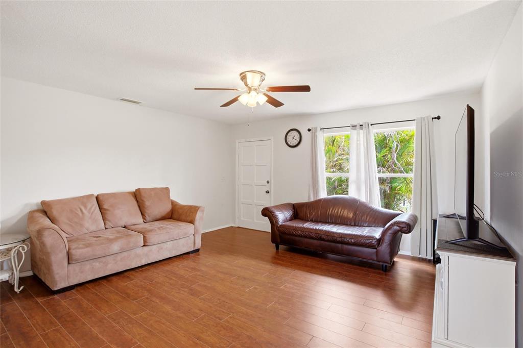A living room features wood-look flooring, two sofas, a ceiling fan, and a television — 213 GRANADA BOULEVARD, NORTH PORT, FL