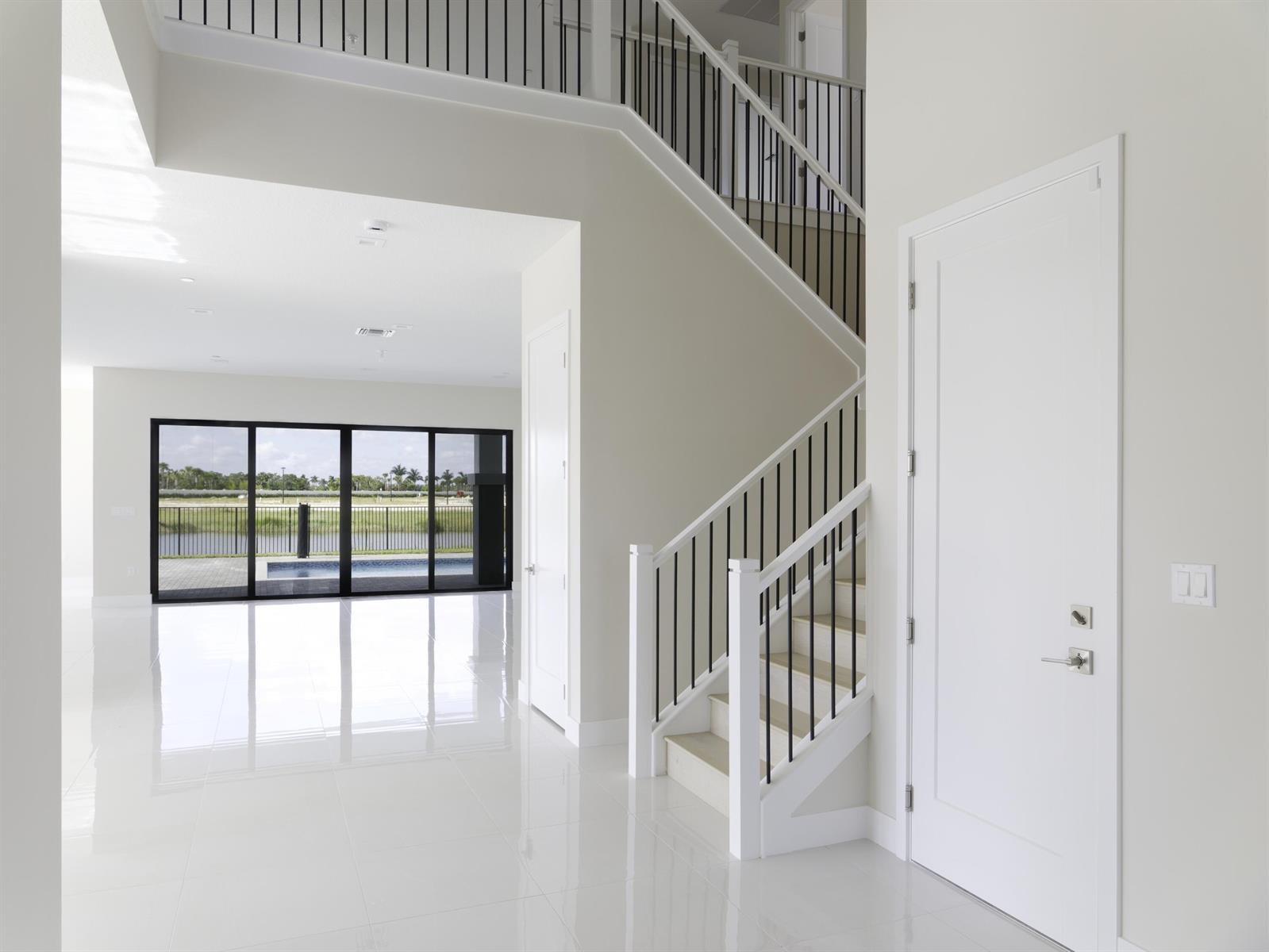 A bright foyer features white tile floors, a staircase with black railings, and glass sliding doors — 9895 Migration Point, Palm Beach Gardens FL 33412, PALM BEACH GARDENS, FL