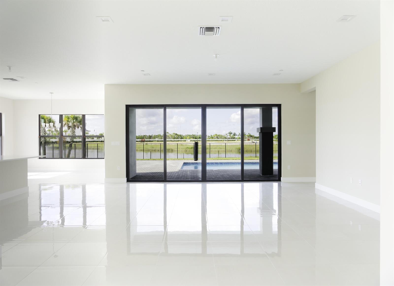 An empty room with white tile floors, recessed lighting, and large sliding glass doors overlooking a pool — 9895 Migration Point, Palm Beach Gardens FL 33412, PALM BEACH GARDENS, FL