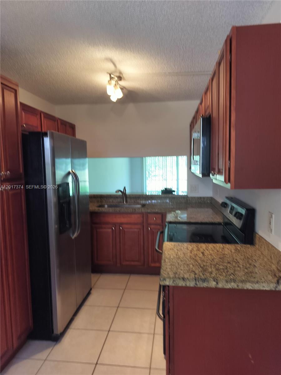 A galley kitchen features wood cabinets, granite countertops, stainless steel appliances, and tile flooring — 1001 Keystone Dr # F, Jupiter FL 33458, JUPITER, FL