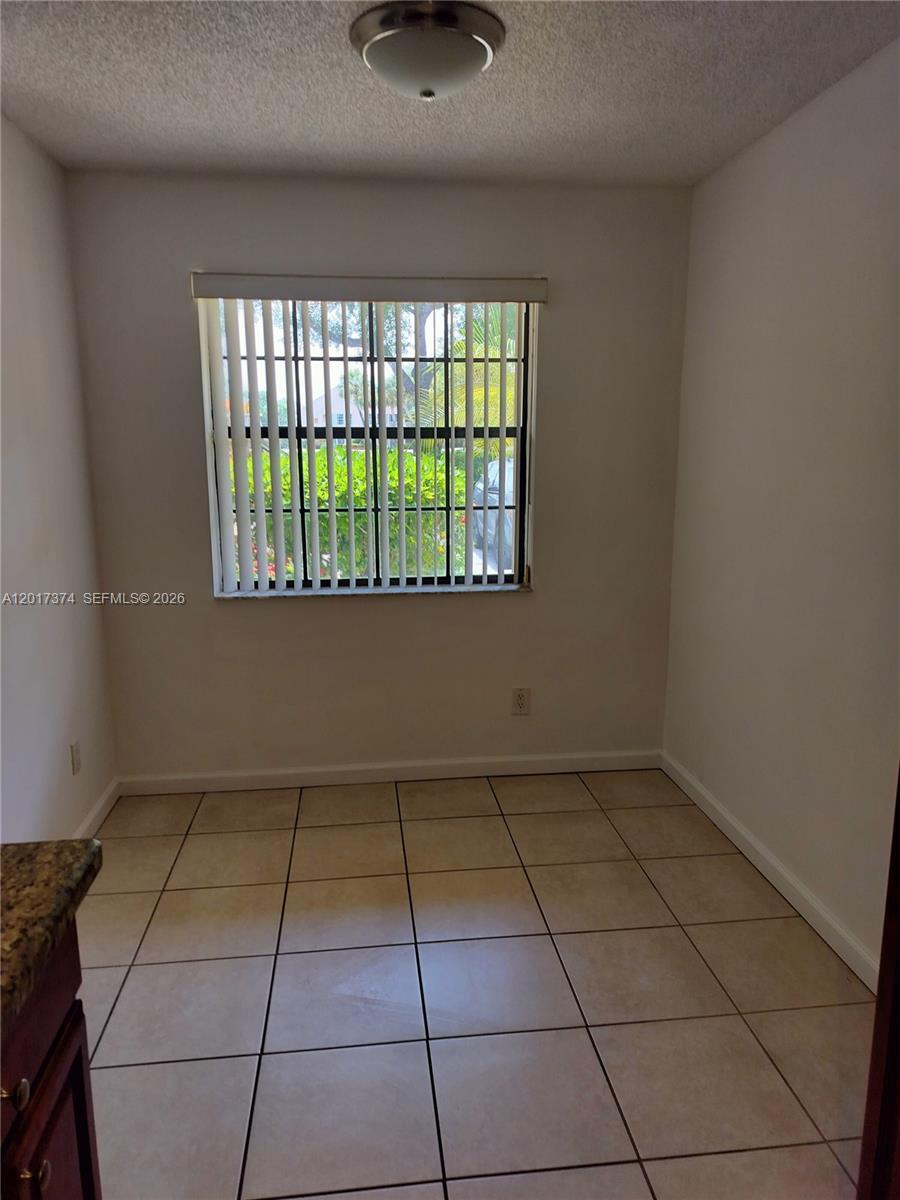 A small, empty room with beige tile flooring, a window with vertical blinds, and a ceiling light — 1001 Keystone Dr # F, Jupiter FL 33458, JUPITER, FL