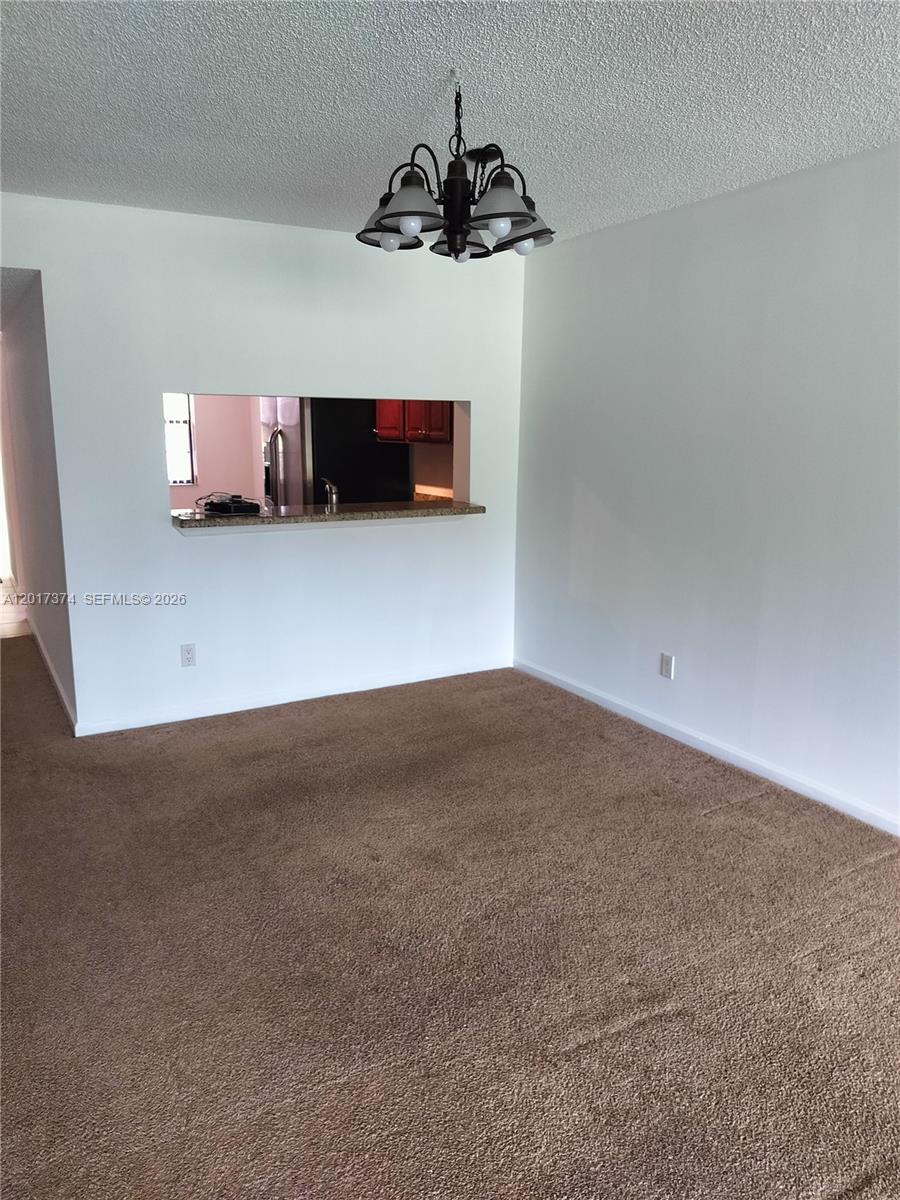 A dining area features brown carpet, a chandelier, and a pass-through window to the kitchen — 1001 Keystone Dr # F, Jupiter FL 33458, JUPITER, FL