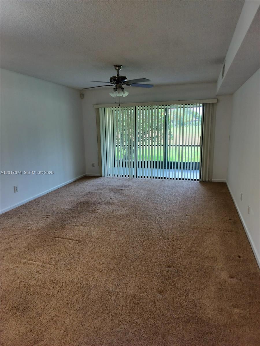 An empty living room features beige carpeting, a ceiling fan, and vertical sliding glass doors — 1001 Keystone Dr # F, Jupiter FL 33458, JUPITER, FL