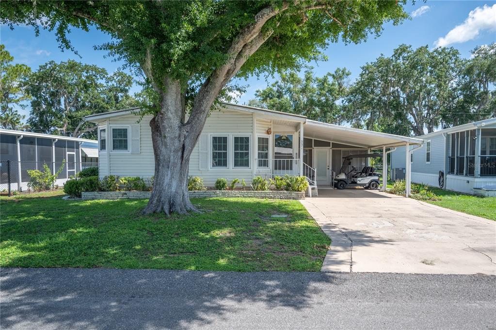 A single-story manufactured home with a large tree, a carport, and a golf cart — 1610 REYNOLDS ROAD UNIT 333, LAKELAND, FL
