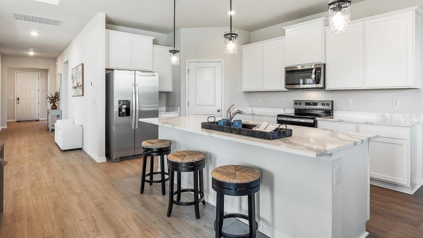 A kitchen features white cabinets, stainless steel appliances, a marble-topped island, and three bar stools — 10425 WOODLAND GARDEN WAY, PARRISH, FL