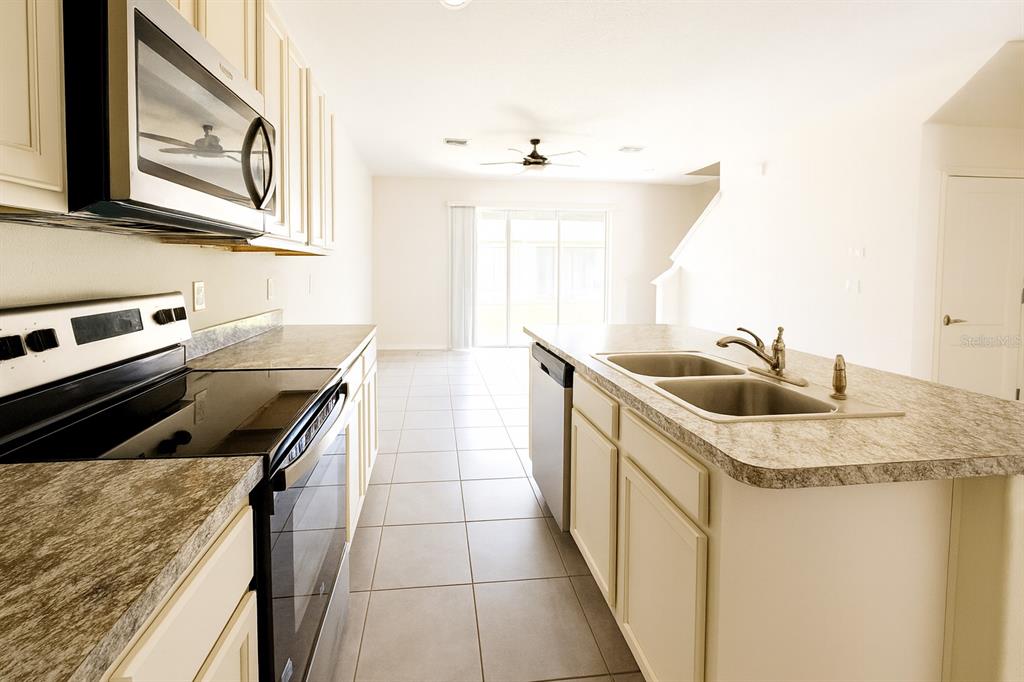 A kitchen with light cabinets, granite-look countertops, stainless steel appliances, and tile flooring — 1288 YELLOW FINCH DRIVE, DAVENPORT, FL