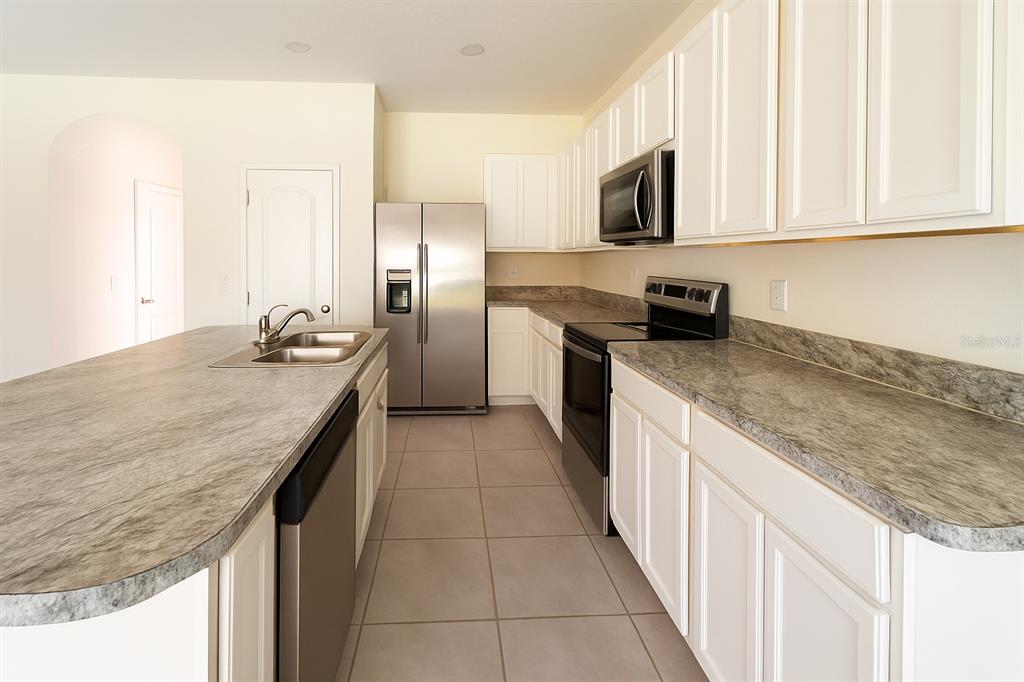 A kitchen features white cabinets, stainless steel appliances, and gray laminate countertops — 1288 YELLOW FINCH DRIVE, DAVENPORT, FL