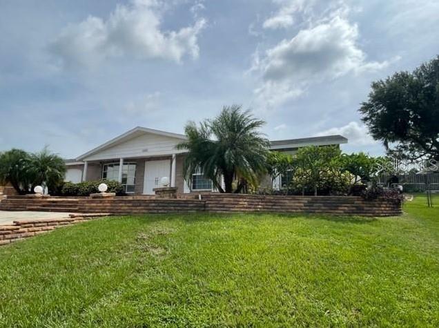 A single-story house features a brick retaining wall, a palm tree, and a grassy lawn — 1326 LAKE ARIANA BOULEVARD, AUBURNDALE, FL