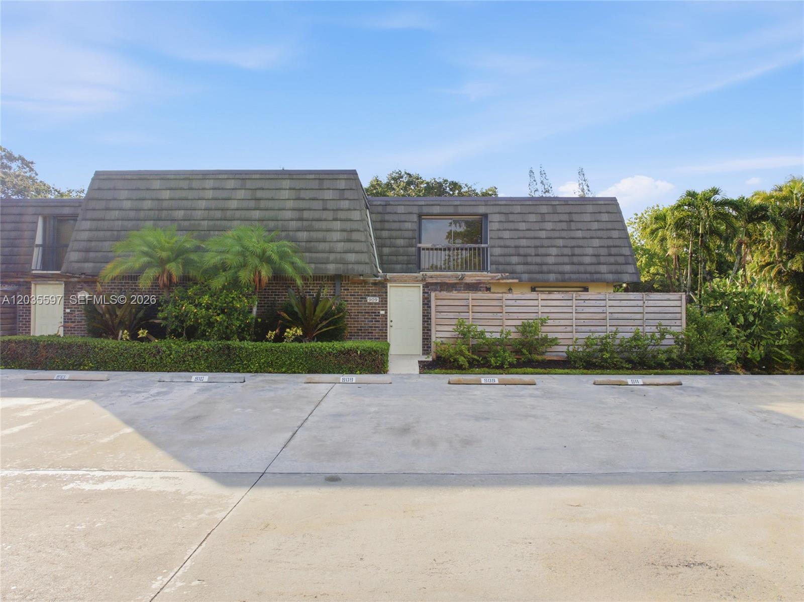 A two-story townhouse exterior features a shingled mansard roof, brick facade, and assigned parking spaces — 909 9th Ter, Palm Beach Gardens FL 33418, PALM BEACH GARDENS, FL