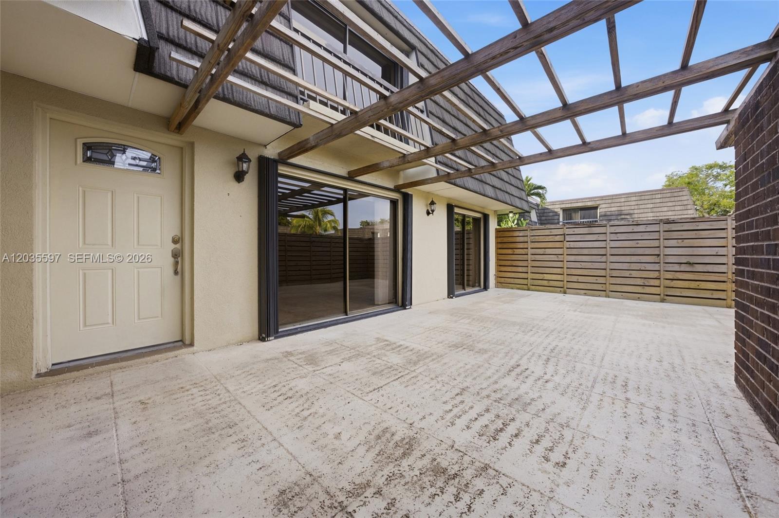 A patio features a wooden pergola, sliding glass doors, and a beige exterior wall — 909 9th Ter, Palm Beach Gardens FL 33418, PALM BEACH GARDENS, FL