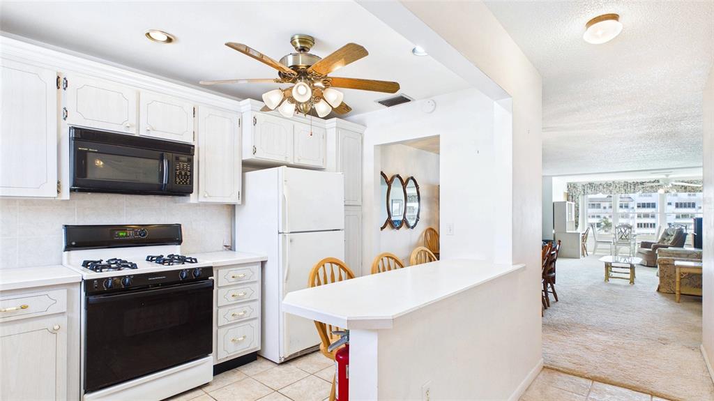 A kitchen with white cabinets, a black stove, and a breakfast bar overlooks a living area — 6025 SHORE BOULEVARD S UNIT 303, GULFPORT, FL