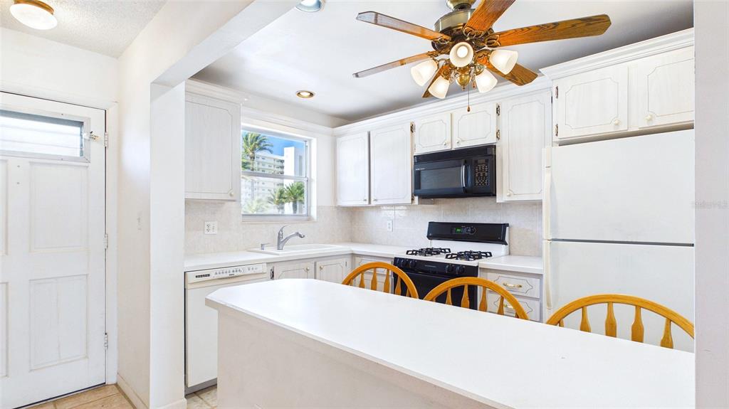A kitchen features white cabinets, a breakfast bar with wooden chairs, and a ceiling fan — 6025 SHORE BOULEVARD S UNIT 303, GULFPORT, FL