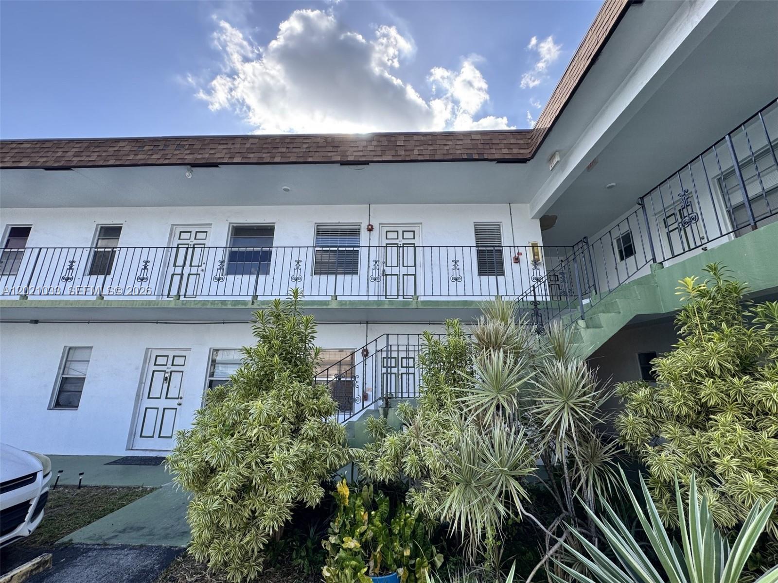 A two-story apartment building features white stucco walls, a brown shingled roof, and metal railings — 2219 Polk St # 4B, Hollywood FL 33020, HOLLYWOOD, FL