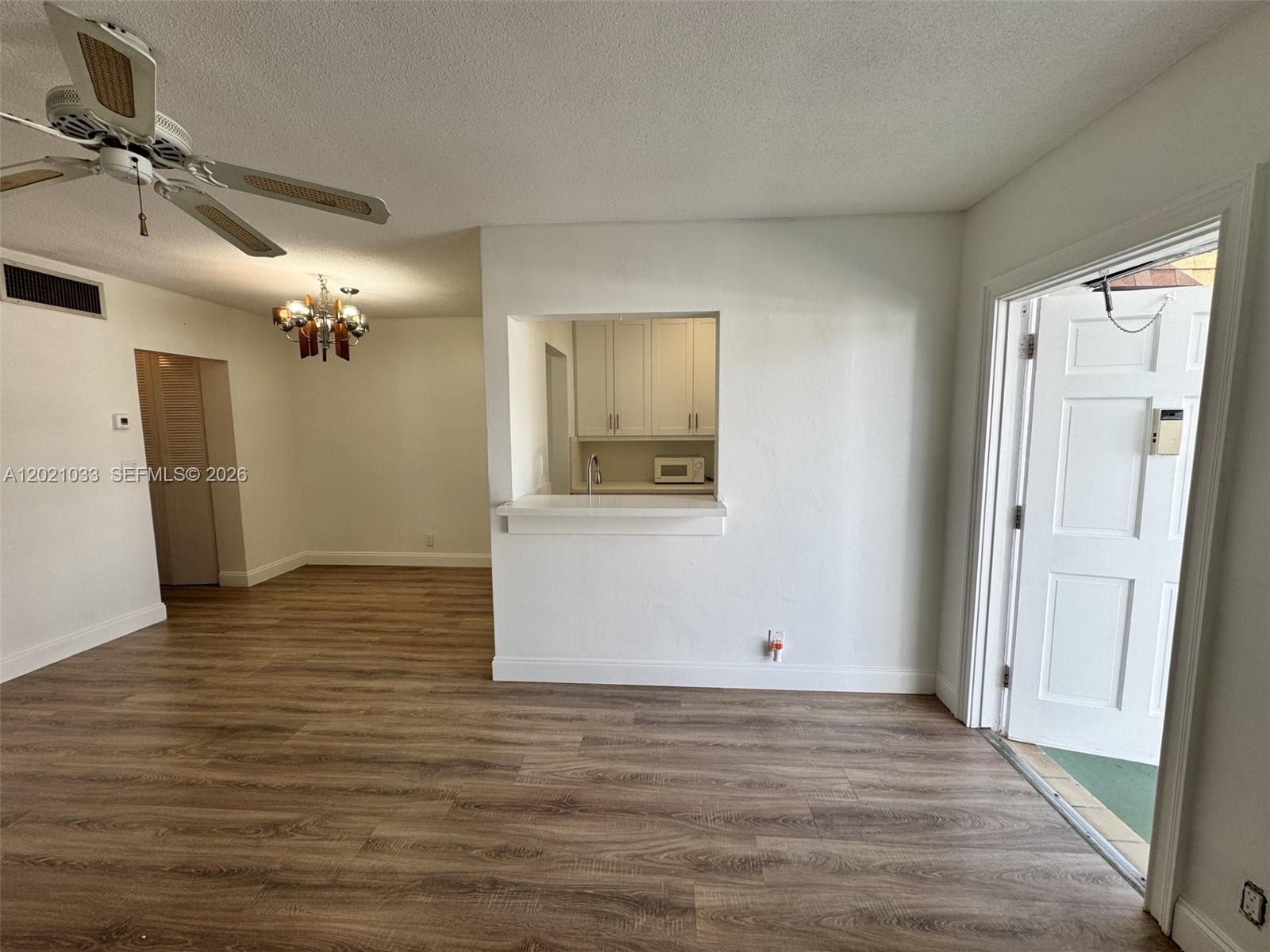 An interior view shows a living area with wood-look flooring, a ceiling fan, and a kitchen pass-through — 2219 Polk St # 4B, Hollywood FL 33020, HOLLYWOOD, FL