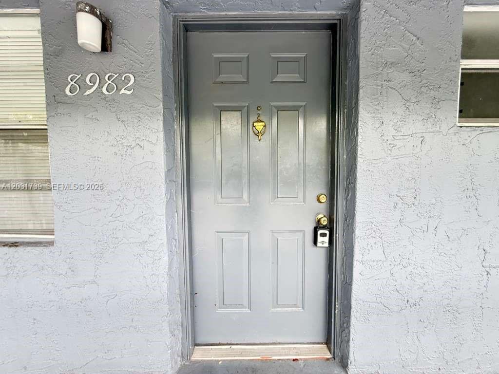 A gray front door with a gold knocker and a lockbox is set in a stucco wall — 8982 W Sample Rd # 204, Coral Springs FL 33065, CORAL SPRINGS, FL