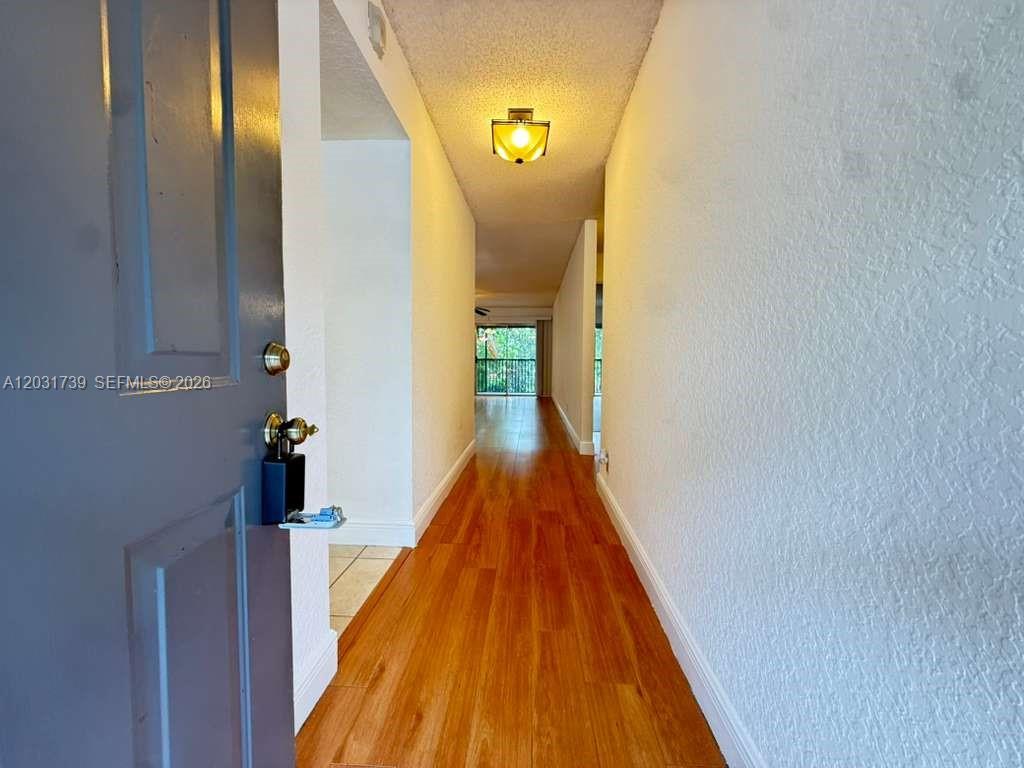 A view from an open doorway looks down a hallway with wood-look flooring — 8982 W Sample Rd # 204, Coral Springs FL 33065, CORAL SPRINGS, FL
