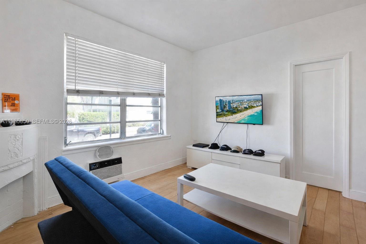 A living room features a blue sofa, white coffee table, wall-mounted television, and hardwood floors — 760 Jefferson Ave # 5, Miami Beach FL 33139, MIAMI BEACH, FL