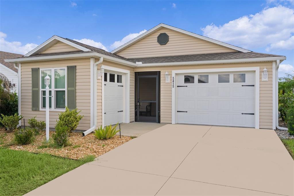 A tan, single-story house with a two-car garage and a front entrance with a screen door — 5415 ZAJAC AVENUE, THE VILLAGES, FL