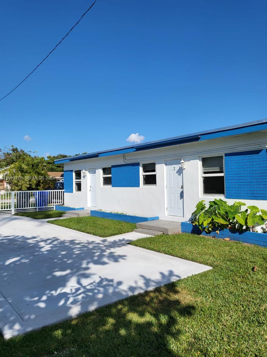 A single-story duplex with white walls, blue accents, and a concrete driveway under a clear sky — HOLLYWOOD, FL