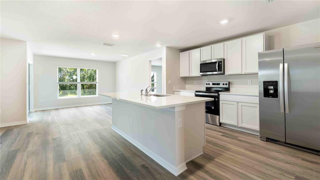 A kitchen with white cabinets, stainless steel appliances, and a large island with quartz countertops — 18308 BEEHIVE TERRACE, BRADENTON, FL