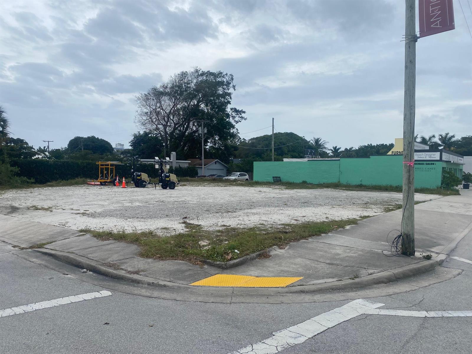 A vacant, gravel-covered corner lot features construction equipment and a green building in the background — 3500 S Dixie Highway, West Palm Beach FL 33405, WEST PALM BEACH, FL