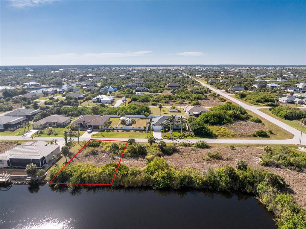 An aerial view shows a vacant waterfront lot outlined in red next to a residential house — 14534 MAYSVILLE CIRCLE, PORT CHARLOTTE, FL