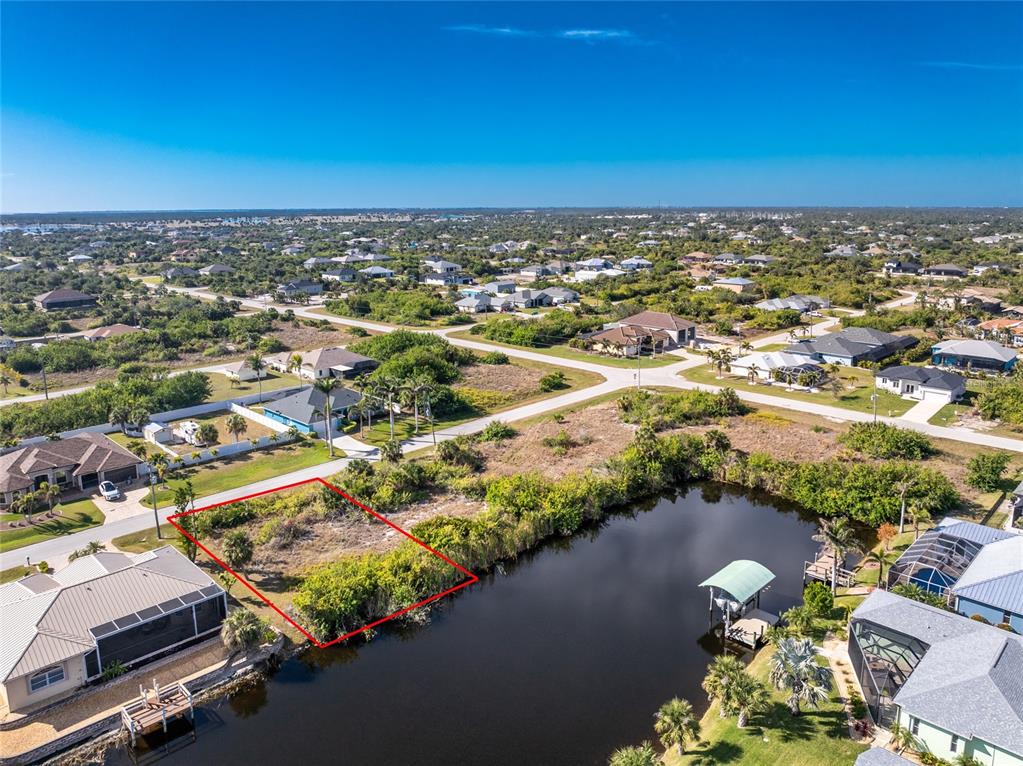 An aerial view shows a vacant, rectangular waterfront lot outlined in red next to houses — 14534 MAYSVILLE CIRCLE, PORT CHARLOTTE, FL