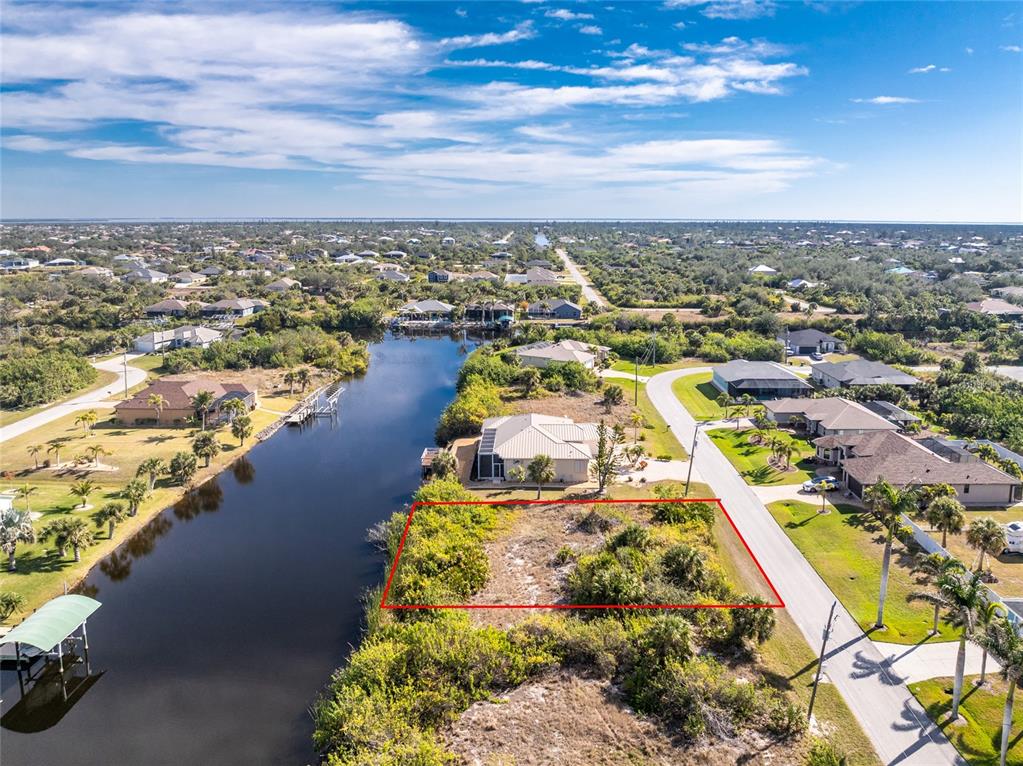 An aerial view shows a vacant waterfront lot outlined in red next to a paved road — 14534 MAYSVILLE CIRCLE, PORT CHARLOTTE, FL