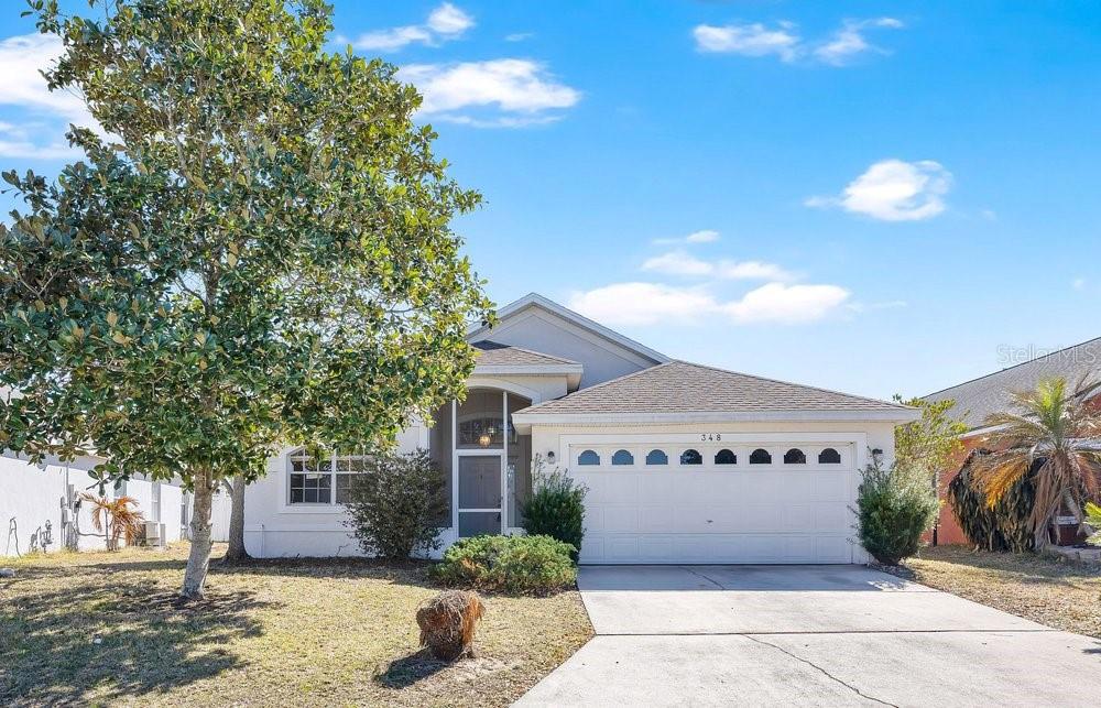 A single-story suburban house with a white exterior, a two-car garage, and a large tree — 348 SIR PHILLIPS DRIVE, DAVENPORT, FL