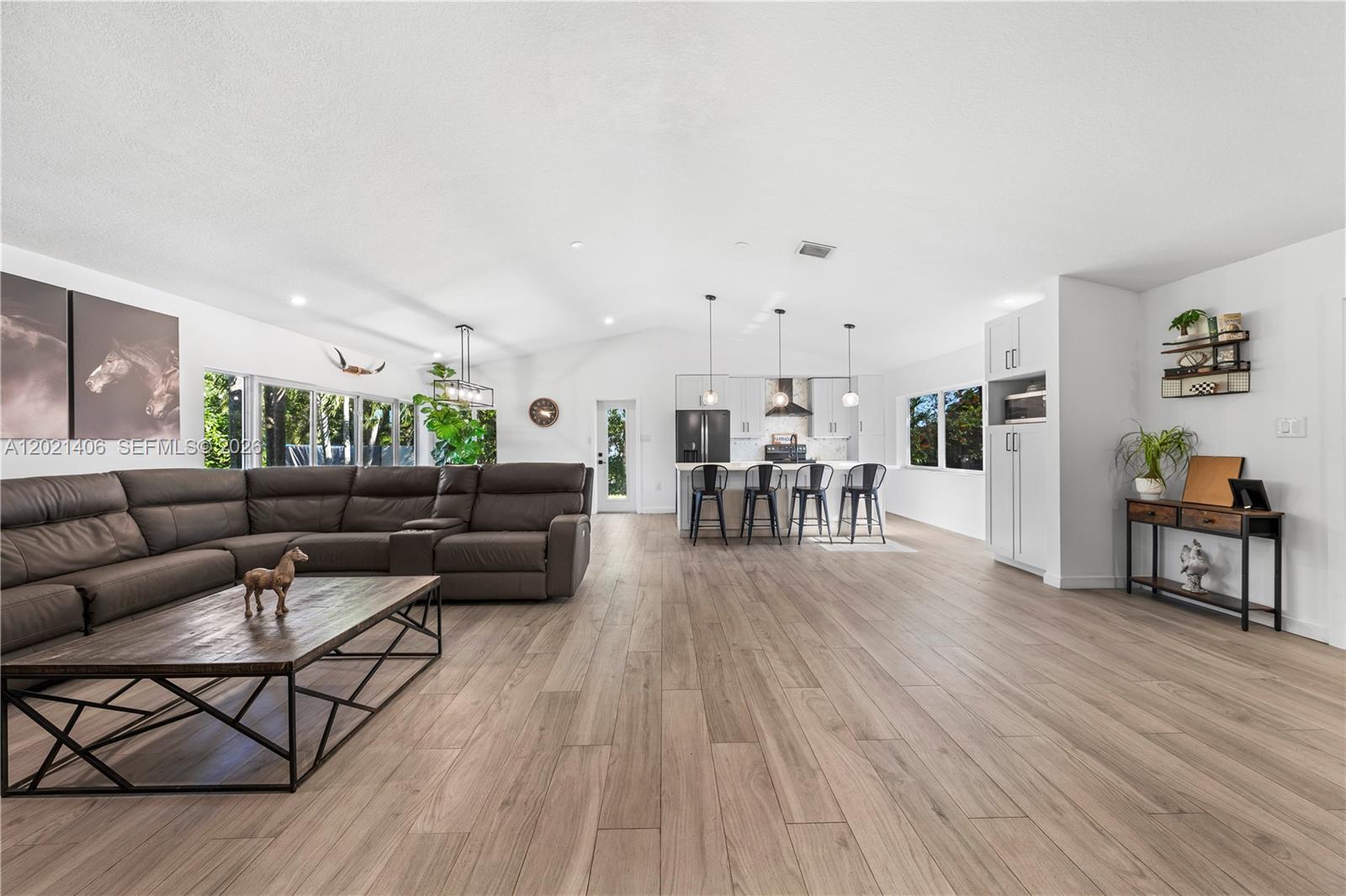 An open-concept living room and kitchen feature light wood flooring, a large sectional, and island seating — 19601 SW 187th Ave, Miami FL 33187, MIAMI, FL