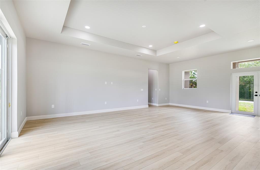 An empty living room features light wood-look flooring, a tray ceiling, and a glass door — 2635 SNUG STREET, NORTH PORT, FL