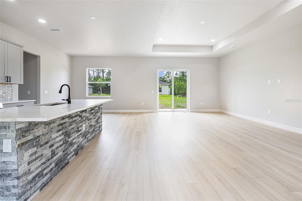 A kitchen with a stone-faced island and light wood flooring opens into a living area — 2635 SNUG STREET, NORTH PORT, FL