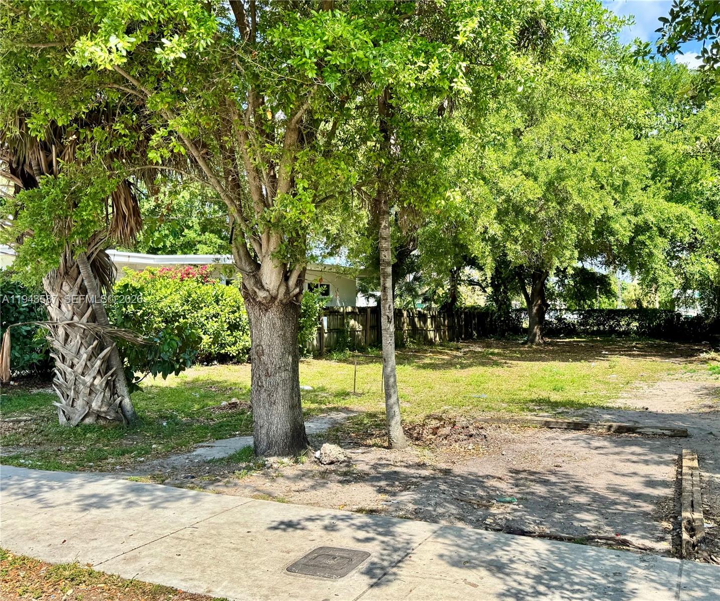 A grassy, tree-filled vacant lot sits behind a concrete sidewalk — 629 NW 65th St, Miami FL 33150, MIAMI, FL