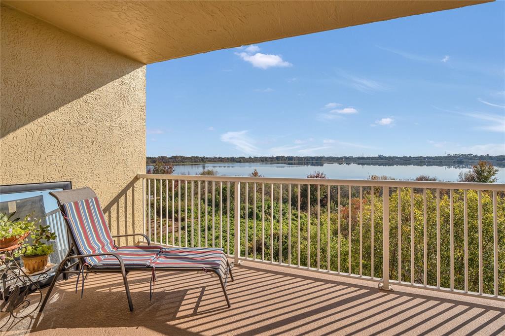 A balcony with a lounge chair overlooks a lake under a clear blue sky — 6336 BUFORD STREET UNIT 405, ORLANDO, FL