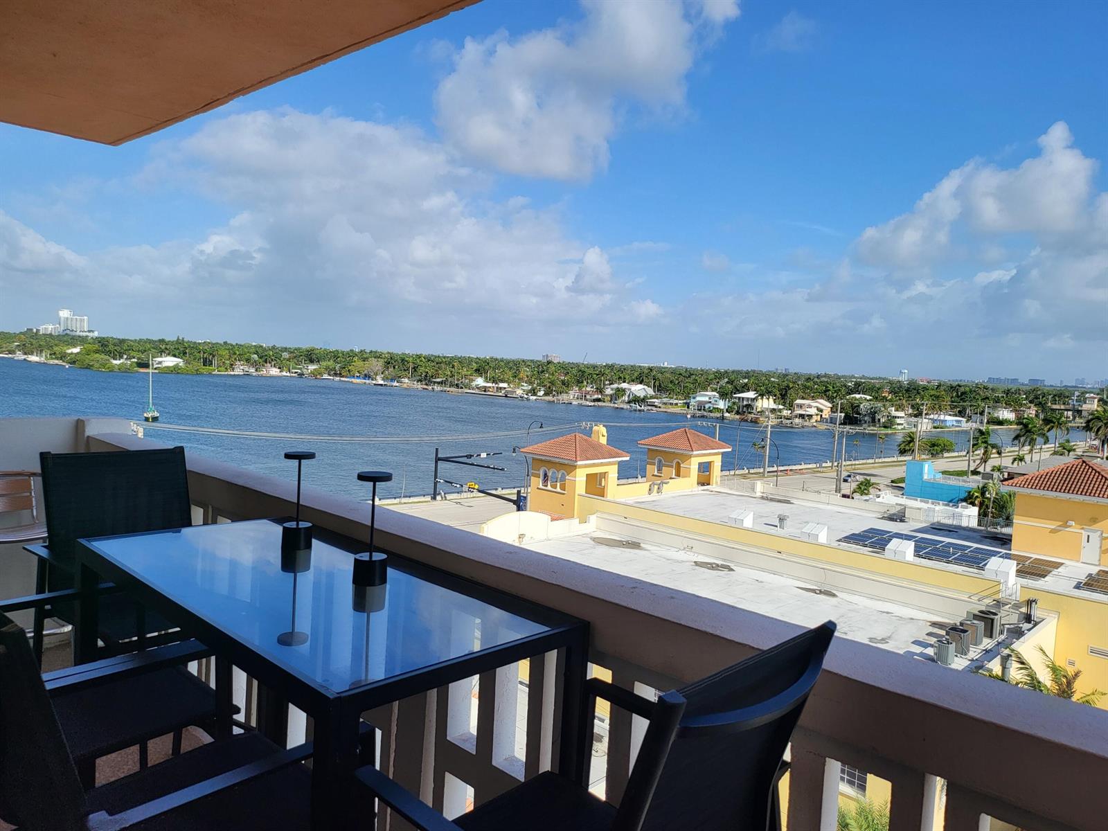 A balcony with a glass-top table and chairs overlooks a waterway and coastal buildings — 801 S Ocean Drive # 805, Hollywood FL 33019, HOLLYWOOD, FL