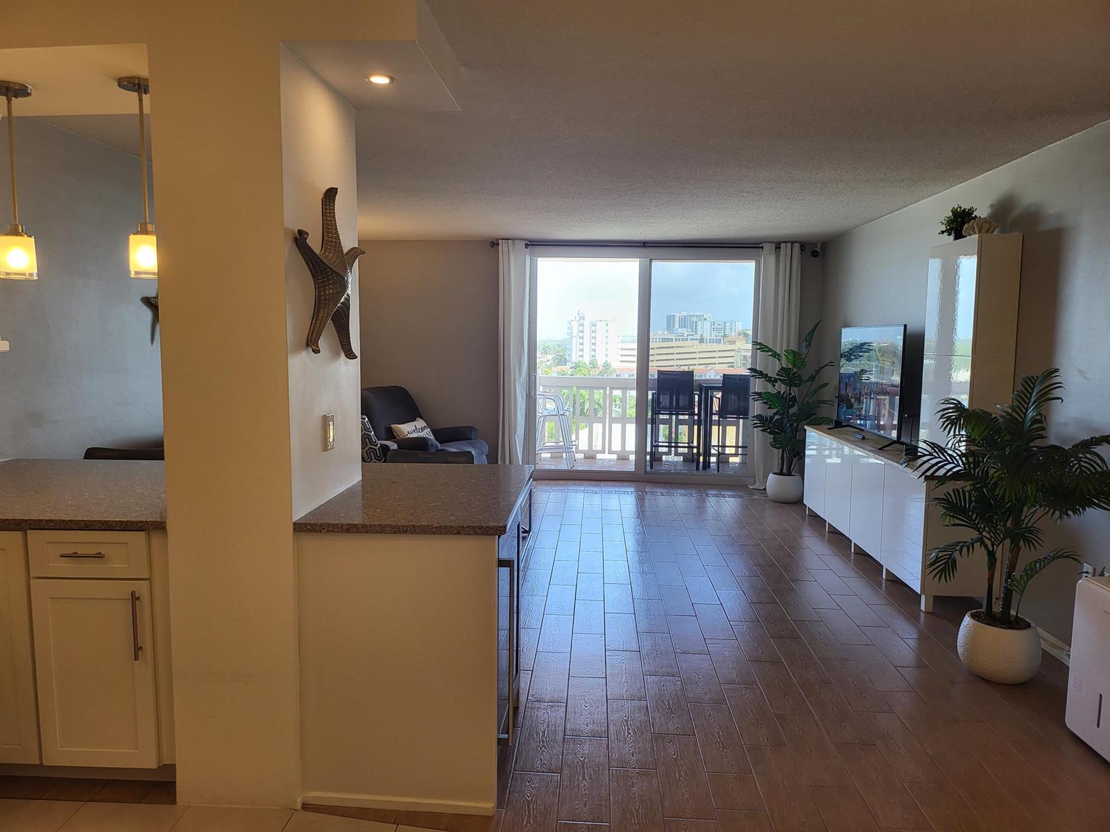 A bright living area features wood-look tile floors, a kitchen peninsula, and a balcony view — 801 S Ocean Drive # 805, Hollywood FL 33019, HOLLYWOOD, FL