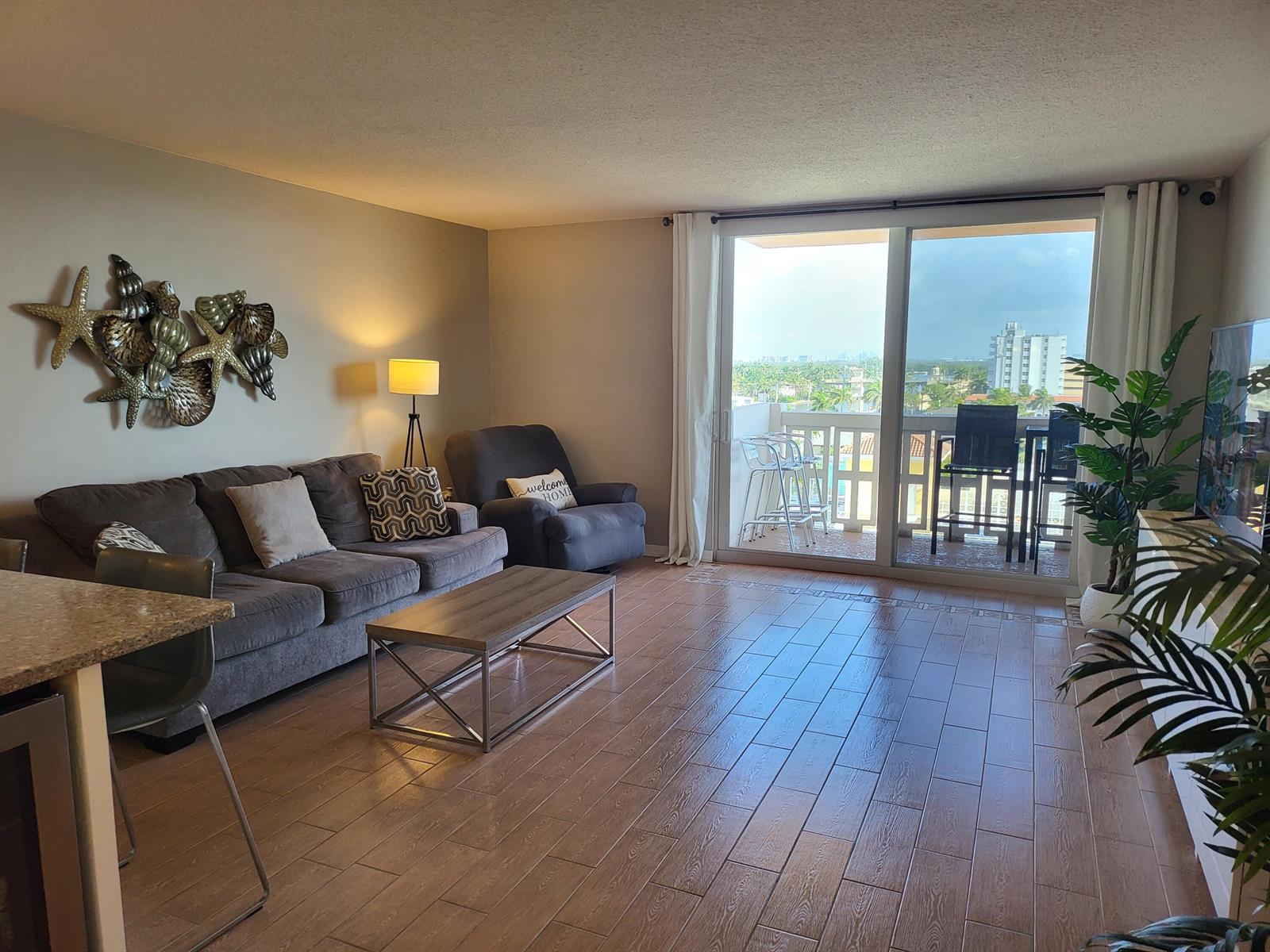 A living room with wood-look tile flooring, a gray sofa, and a balcony with city views — 801 S Ocean Drive # 805, Hollywood FL 33019, HOLLYWOOD, FL