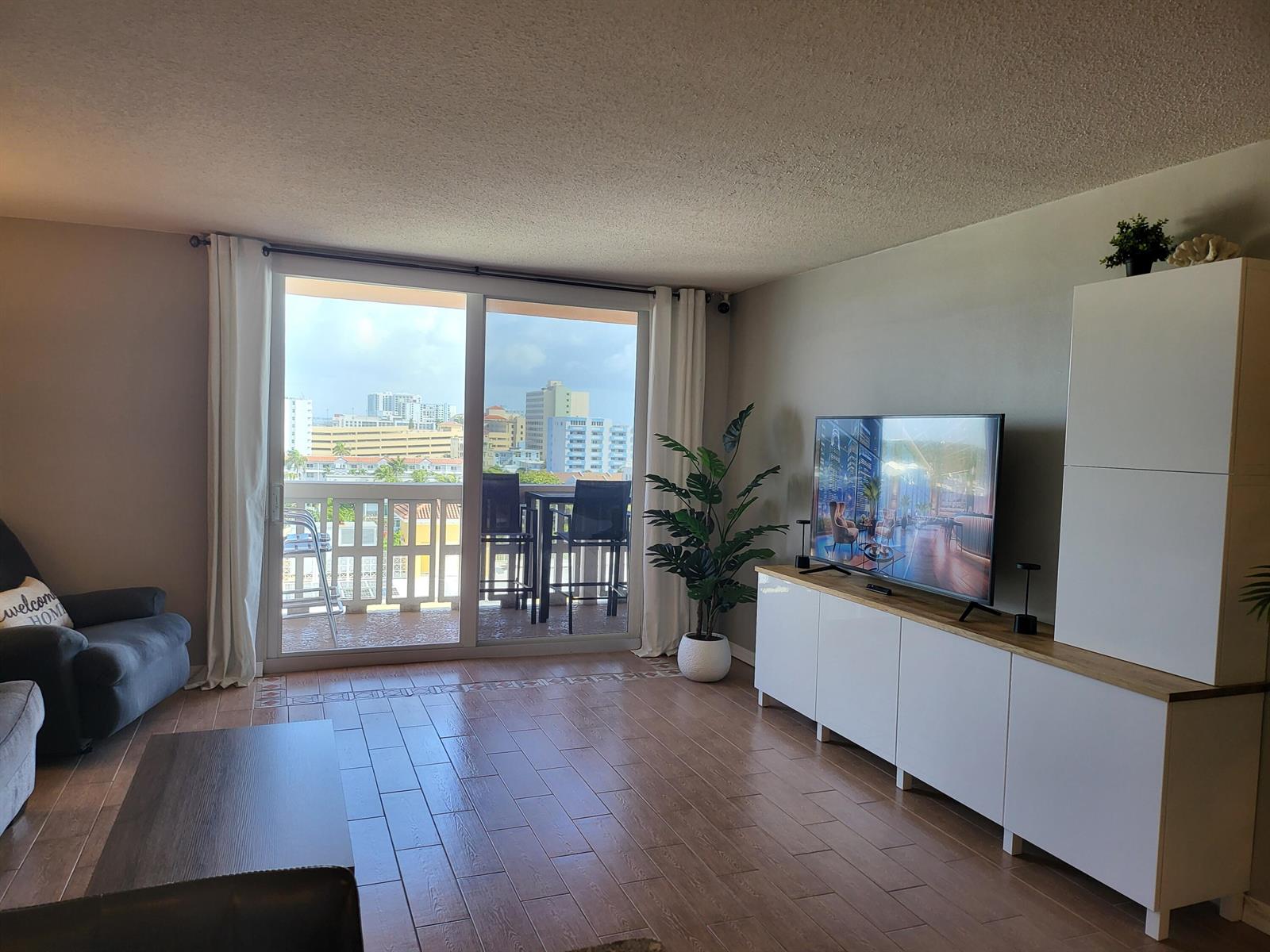 A living room with tile floors, a media console, a television, and a balcony view — 801 S Ocean Drive # 805, Hollywood FL 33019, HOLLYWOOD, FL