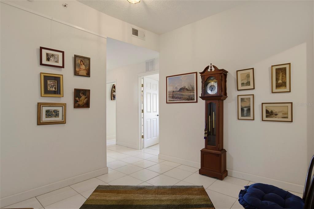 A hallway with white tile floors, a grandfather clock, and several framed pictures on walls — 6312 BUFORD STREET UNIT 708, ORLANDO, FL