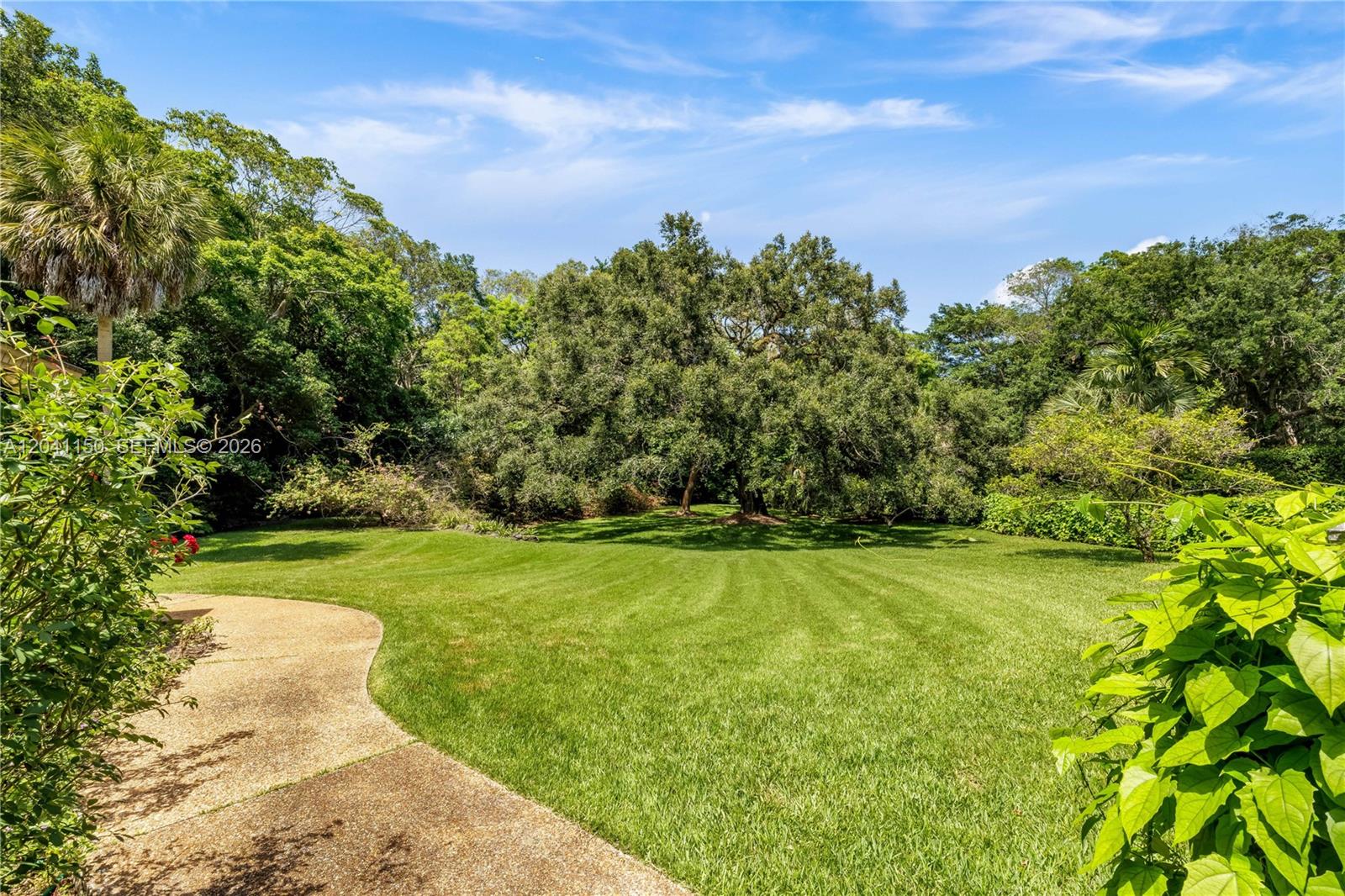 A curved concrete walkway leads through a grassy lawn toward a dense wooded area — 9979 Fairchild Way, Coral Gables FL 33156, CORAL GABLES, FL