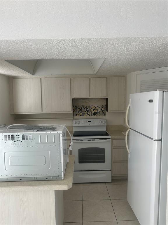 A kitchen with light wood cabinets, white appliances, a tiled floor, and a microwave on the counter — 4158 TAMIAMI TRAIL UNIT B1, PORT CHARLOTTE, FL