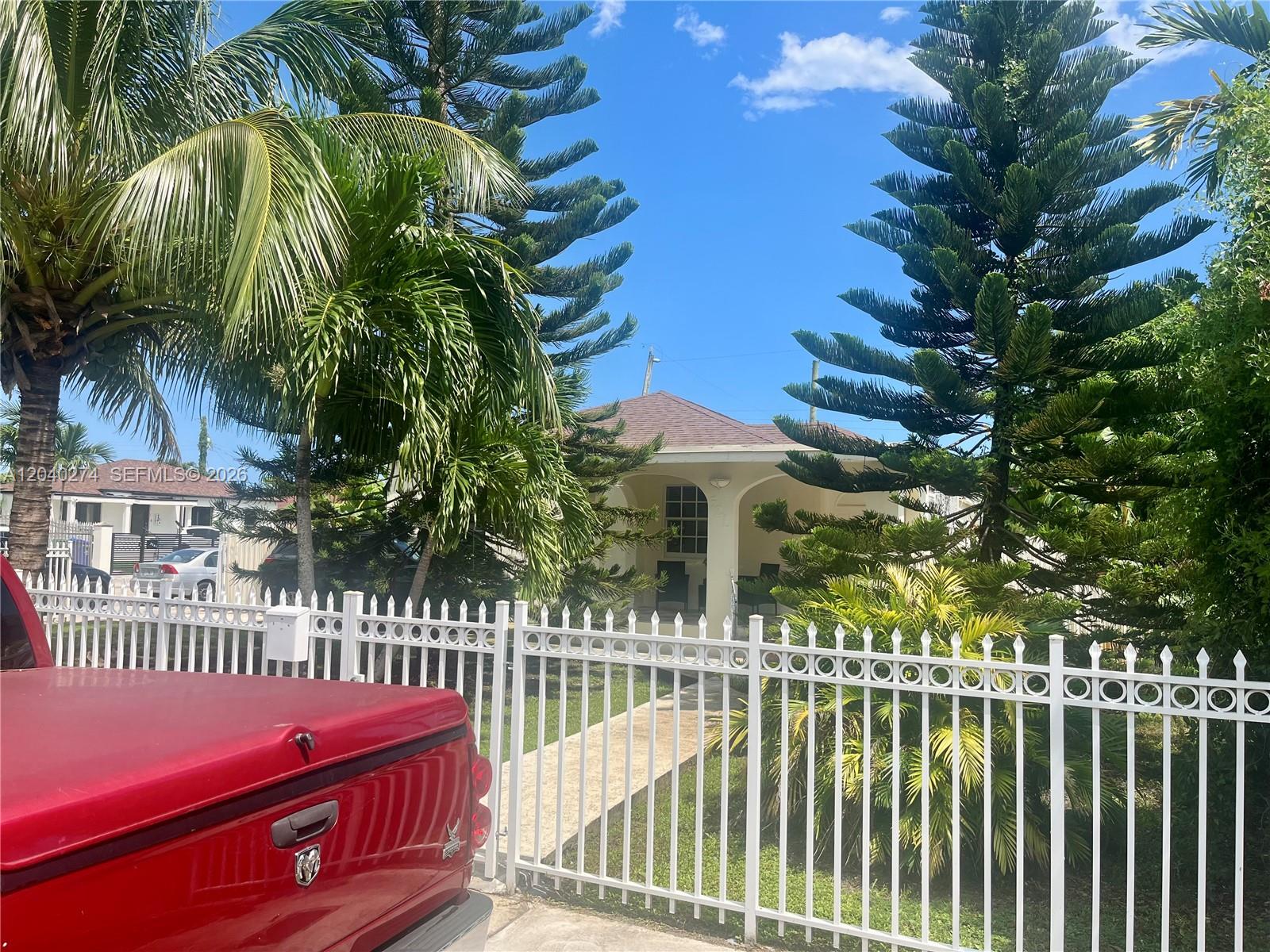 A white fence stands in front of a house surrounded by tall pine trees — 521 NW 32nd Pl, Miami FL 33125, MIAMI, FL