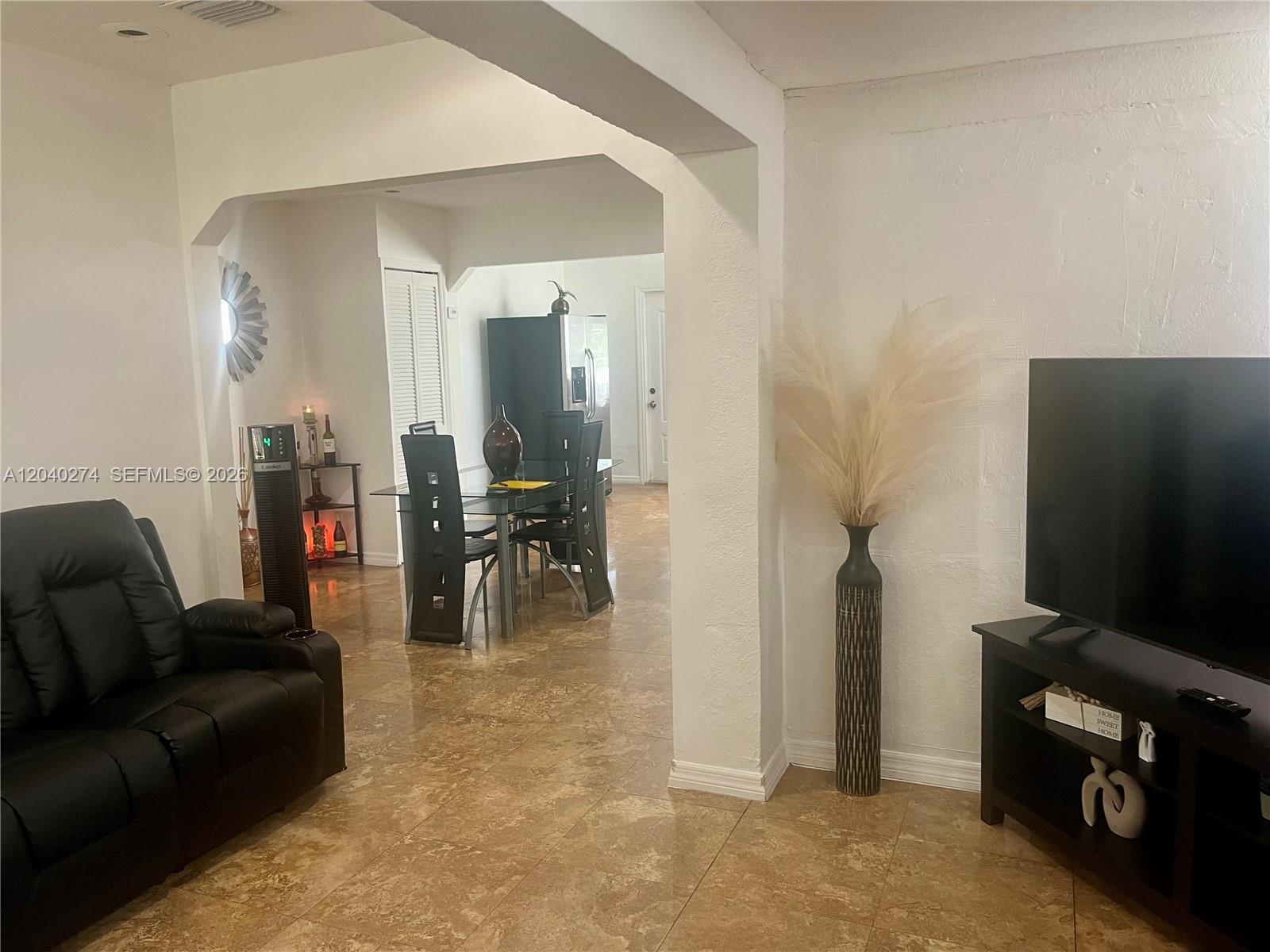 A living room with tile floors leads into a dining area through a wide archway — 521 NW 32nd Pl, Miami FL 33125, MIAMI, FL