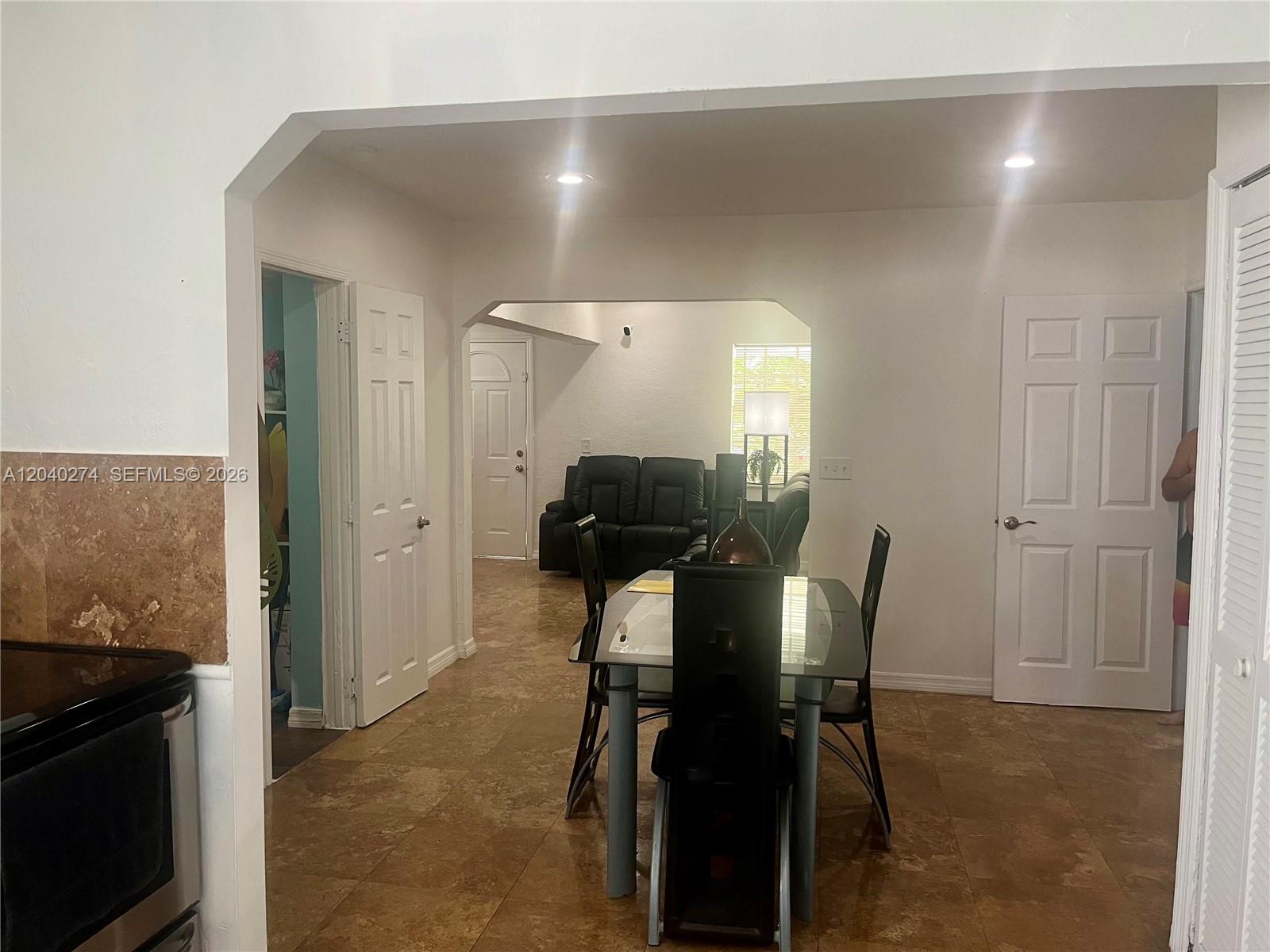 A dining area with a glass table and chairs leads into a living room — 521 NW 32nd Pl, Miami FL 33125, MIAMI, FL