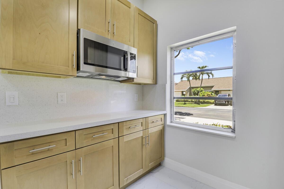 A kitchen features light wood cabinets, a stainless steel microwave, and a window view outside — 8157 Springtree Road, Boca Raton FL 33496, BOCA RATON, FL