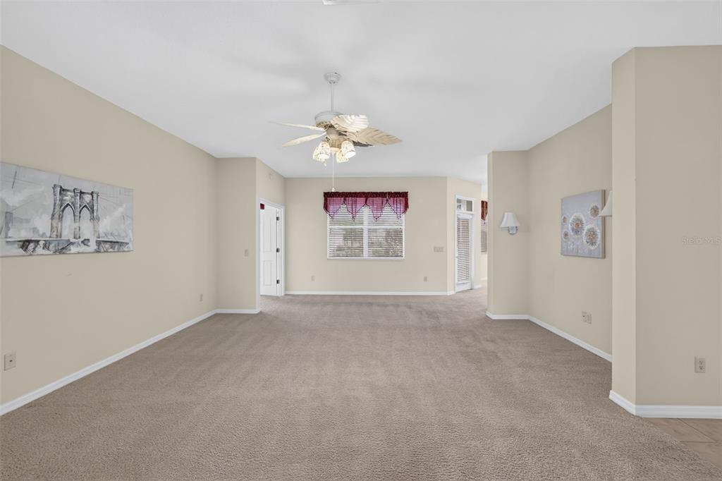 A carpeted living room features a ceiling fan, a window with a valance, and wall art — 2693 IRIS WAY, THE VILLAGES, FL