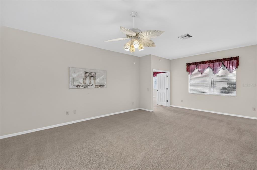 A spacious bedroom features beige carpeting, neutral walls, a ceiling fan, and a window with valances — 2693 IRIS WAY, THE VILLAGES, FL