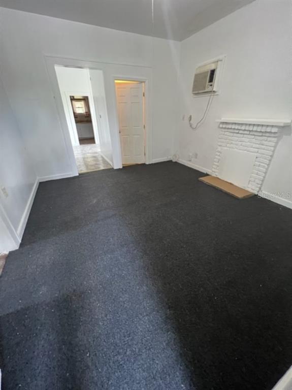 A living room with dark carpeting, a white brick fireplace, and a window air conditioner — 1031 N FLORENCE AVENUE, LAKELAND, FL