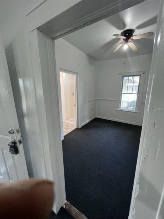 A view through a doorway into a bedroom with dark carpet, white walls, and ceiling fan — 1031 N FLORENCE AVENUE, LAKELAND, FL