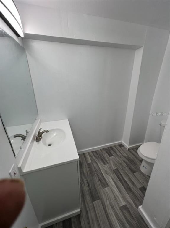 A small bathroom features a white vanity, a mirror, and a toilet on wood-look flooring — 1031 N FLORENCE AVENUE, LAKELAND, FL